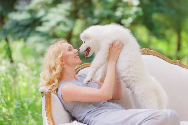 여름 정원에서 복고풍 소파에 그녀의 팔에 흰색 강아지와 함께 아름 다운 소녀 — 스톡 사진