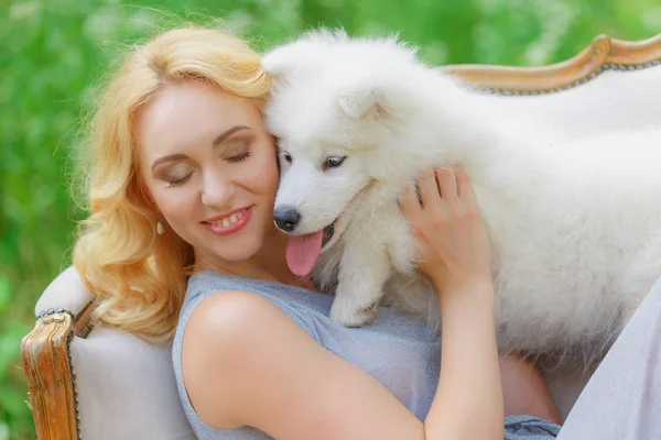 Güzel genç kız ile bir yaz bahçesinde bir retro Divan kucağında beyaz bir köpek yavrusu