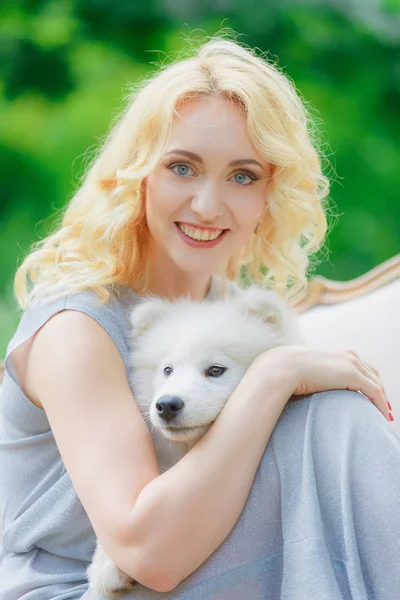 Blond meisje ligt buiten met een witte hond in handen — Stockfoto