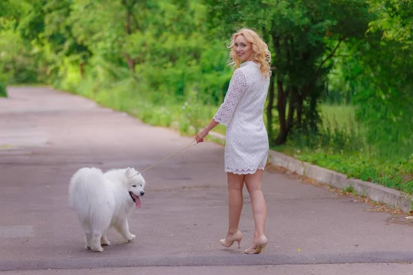 Güzel sarışın kız yürümek yaz bahçesinde beyaz tüylü bir köpek ile elbise