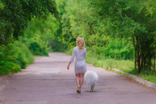 Güzel sarışın kız yürümek yaz bahçesinde beyaz tüylü bir köpek ile elbise