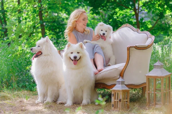 Bella ragazza con un cucciolo bianco tra le braccia e vecchi cani bianchi morbidi su un divano retrò in un giardino estivo Foto Stock