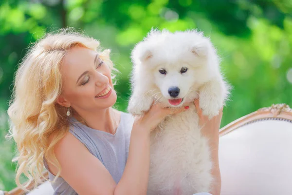 Bella ragazza con un cucciolo bianco tra le braccia su un divano retrò in un giardino estivo Immagine Stock