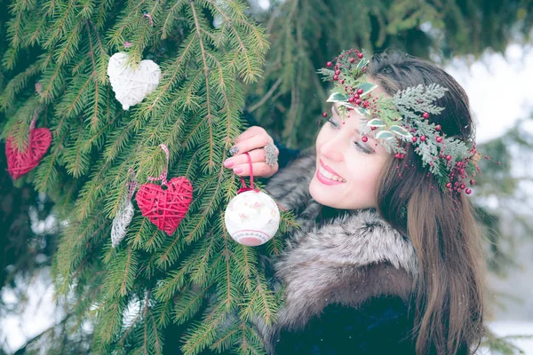 Portret van mooie jonge lachende vrouw versieren van een kerstboom buiten op een koude winterdag. — Stockfoto
