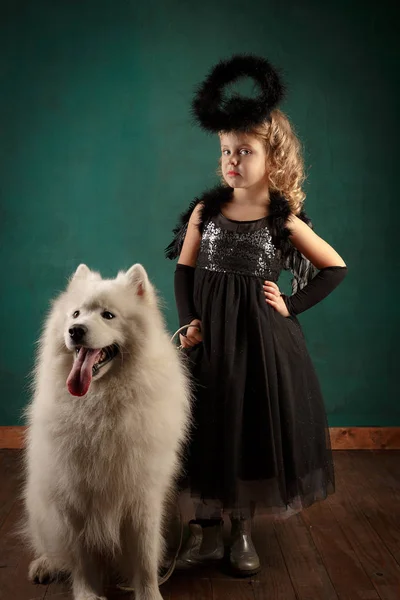 Composição de Ano Novo no estúdio. Loira bonito pouco em um traje de anjo preto com um grande cão branco. Ano do cão, Humor — Fotografia de Stock
