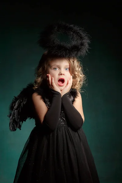 Demone per bambini con ali nere in costume di carnevale e stile religioso in studio con un'emozione interessante . Foto Stock