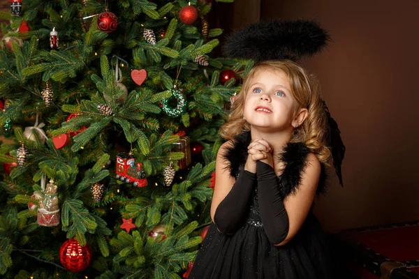 Pregate una bambina in costume da angelo nero, guardando con speranza per la pace. Buona infanzia e pace. Natale, Capodanno Foto Stock Royalty Free