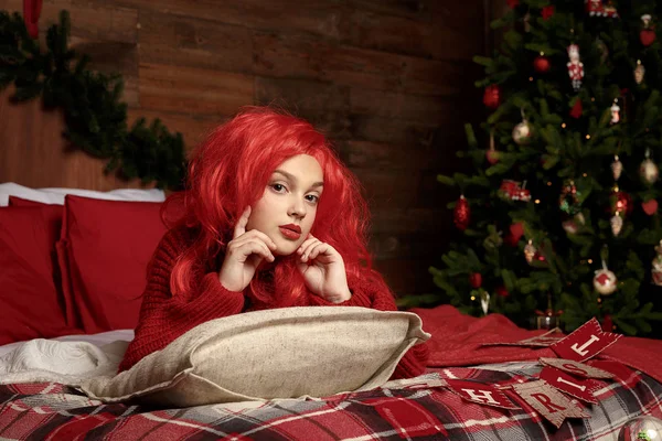 Ενός έφηβου κοριτσιού σε μια κόκκινη περούκα έγκειται στο κρεβάτι σε ένα δωμάτιο για τα Χριστούγεννα. Μόδα, νέα χρονιά — Φωτογραφία Αρχείου