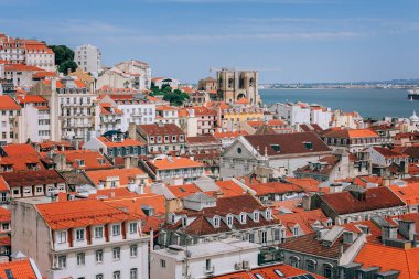 Arkasında dağ olan büyük turuncu bir bina. Lizbon 'daki bir gözlem güvertesinden çatı ve okyanus manzarası. Portekiz