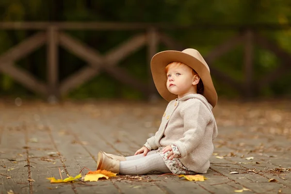 Red-haired baby girl in a hat sitting on the street in autumn — Stock Photo, Image