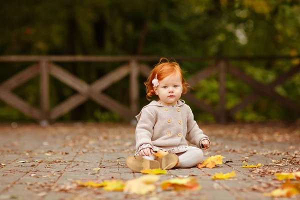 निसर्गाच्या पार्श्वभूमीवर लाल केस असलेली बाळ मुलगी आणि बसली — स्टॉक फोटो, इमेज