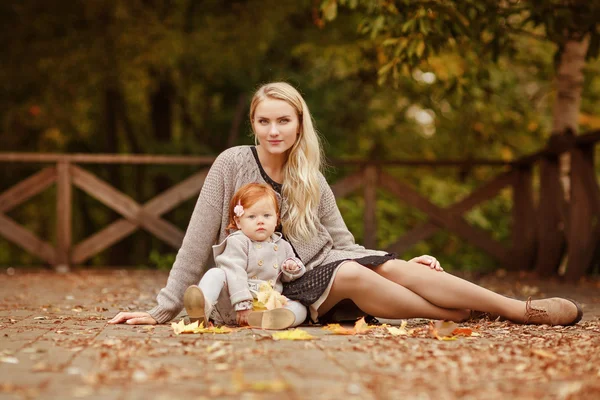 Mutti umarmt das rothaarige Babymädchen auf dem Herbstwald-Rücken sanft — Stockfoto