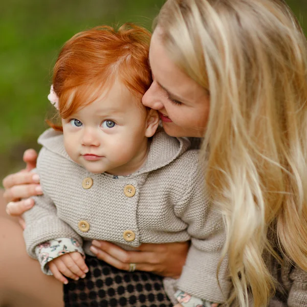 Mutti umarmt das rothaarige Babymädchen auf dem Herbstwald-Rücken sanft — Stockfoto