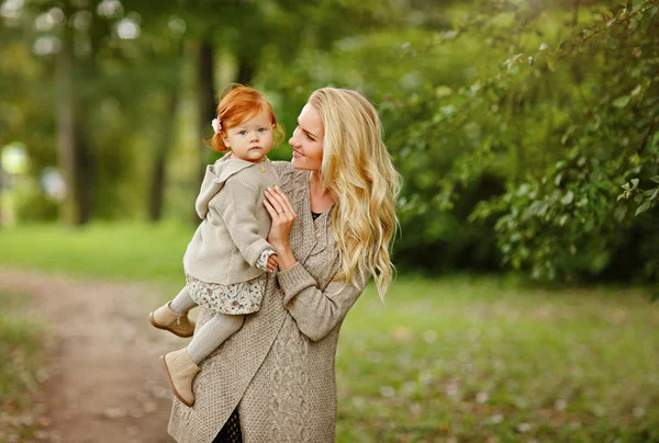 秋の森の背景の赤毛の女の赤ちゃんをやさしく包みこむママ — ストック写真