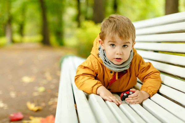 Niño adorable con chaqueta amarilla acostado en un banco a la par — Foto de Stock