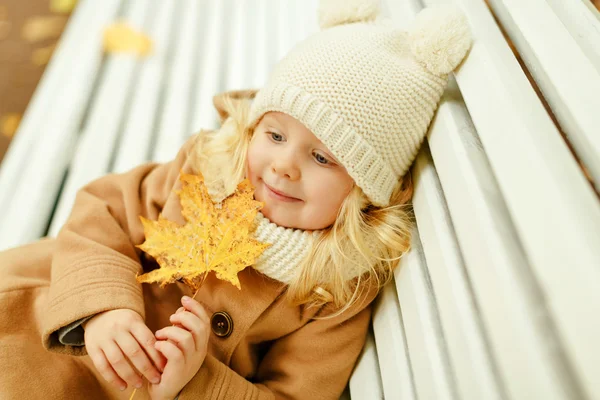 Mooi meisje in een beige jas zittend op een bankje en holdin — Stockfoto