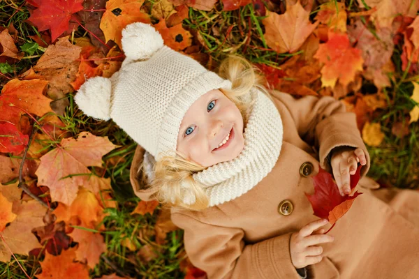 Fetiță drăguță într-o haină bej întinsă pe frunze toamna — Fotografie, imagine de stoc