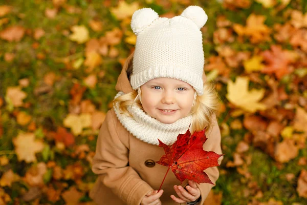 Маленька красива дівчинка в бежевому пальто посміхається в осінньому парку, близько — стокове фото