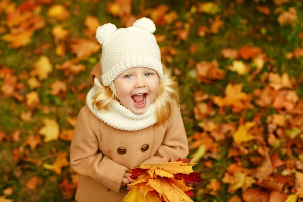 Pequena menina bonita em um casaco bege ri em um parque no outono, c — Fotografia de Stock