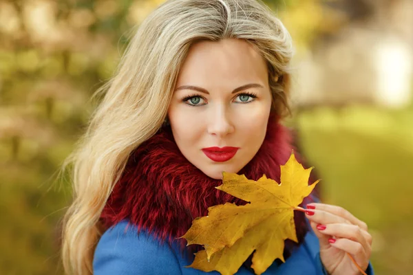 Luxus blonde Mädchen mit schönen Haaren in einem Mantel hält einen Ahorn — Stockfoto