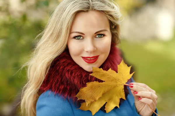 Luxus blonde Mädchen mit schönen Haaren in einem Mantel hält einen Ahorn — Stockfoto
