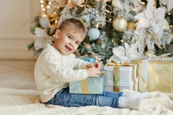 O pequeno menino encantador senta-se perto de uma árvore de Natal com gif — Fotografia de Stock