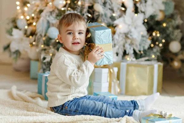 El encantador bebé niño se sienta cerca de un árbol de Navidad con gif — Foto de Stock