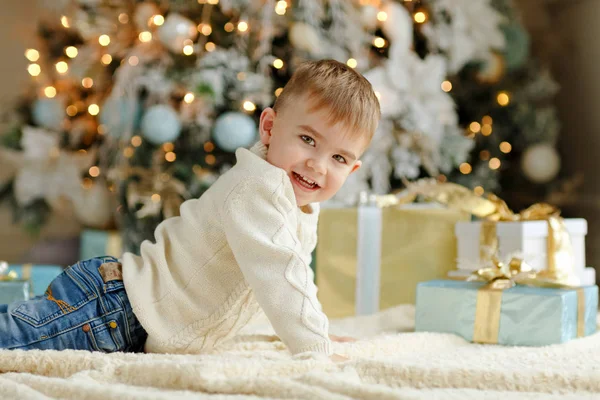 Fermecătorul băieţel stă lângă un pom de Crăciun şi miroase — Fotografie, imagine de stoc