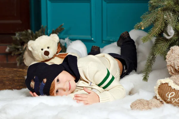 Menino de chapéu sorri e se deita na neve em um estúdio de Natal — Fotografia de Stock