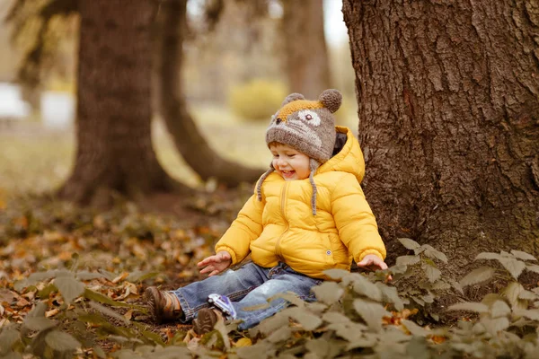 Baby jongetje in gele jas glimlacht in het najaar, zittend onder — Stockfoto