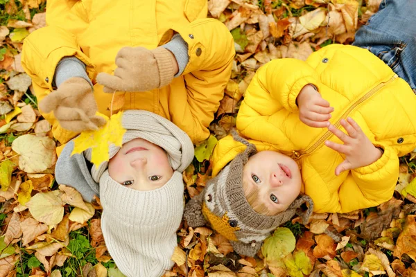 Twee broers in gele jassen herfstbladeren liggen op — Stockfoto