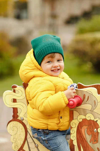 Baby jongetje in gele jas glimlacht in het najaar op de auto — Stockfoto
