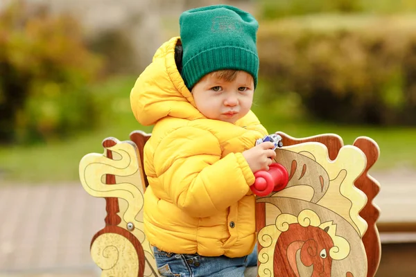 Baby jongetje in gele jas glimlacht in het najaar op de auto — Stockfoto