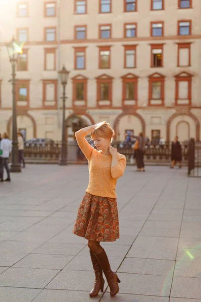 Рыжая девушка в юбке гуляет по городу в солнечный день — стоковое фото