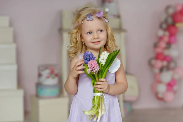 Charming little girl blonde in a dress is holding flowers and sm — Stock Photo, Image