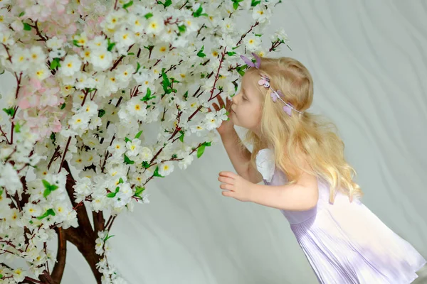 Encantadora niña rubia alcanza para un árbol en flor en una l —  Fotos de Stock