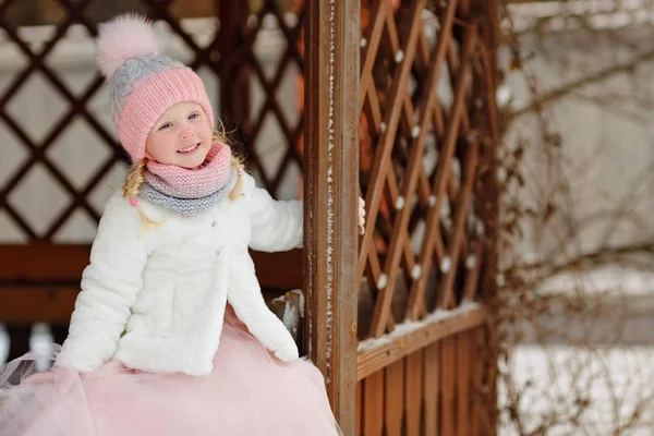 A little girl in a pink skirt in winter smiles in a park in a ga — Stock Photo, Image