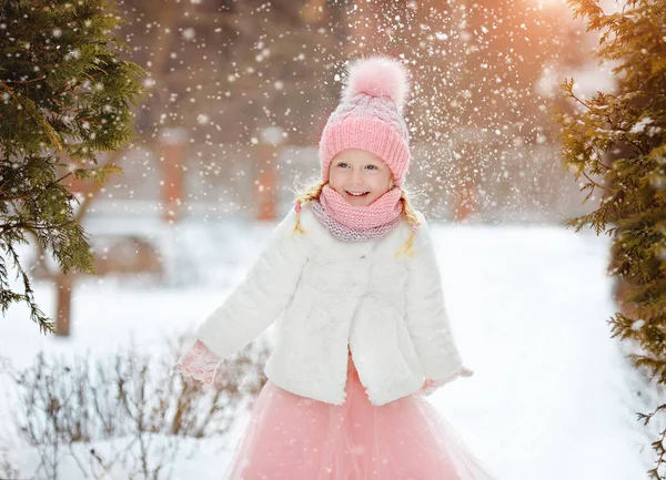 Little girl in a pink skirt in winter smiles in the park and thr — Stock Photo, Image