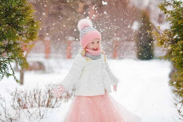 Little girl in a pink skirt in winter smiles in the park and thr — Stock Photo, Image