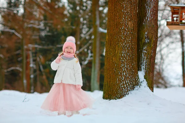 Little girl in a pink skirt in winter smiles in the park — Stock Photo, Image