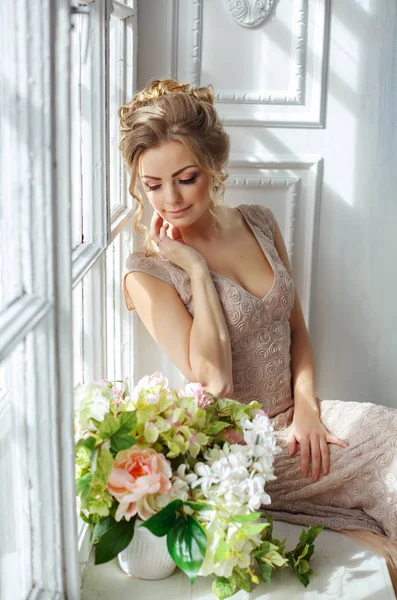 Una hermosa mujer rubia sensual con un vestido beige se sienta en un —  Fotos de Stock