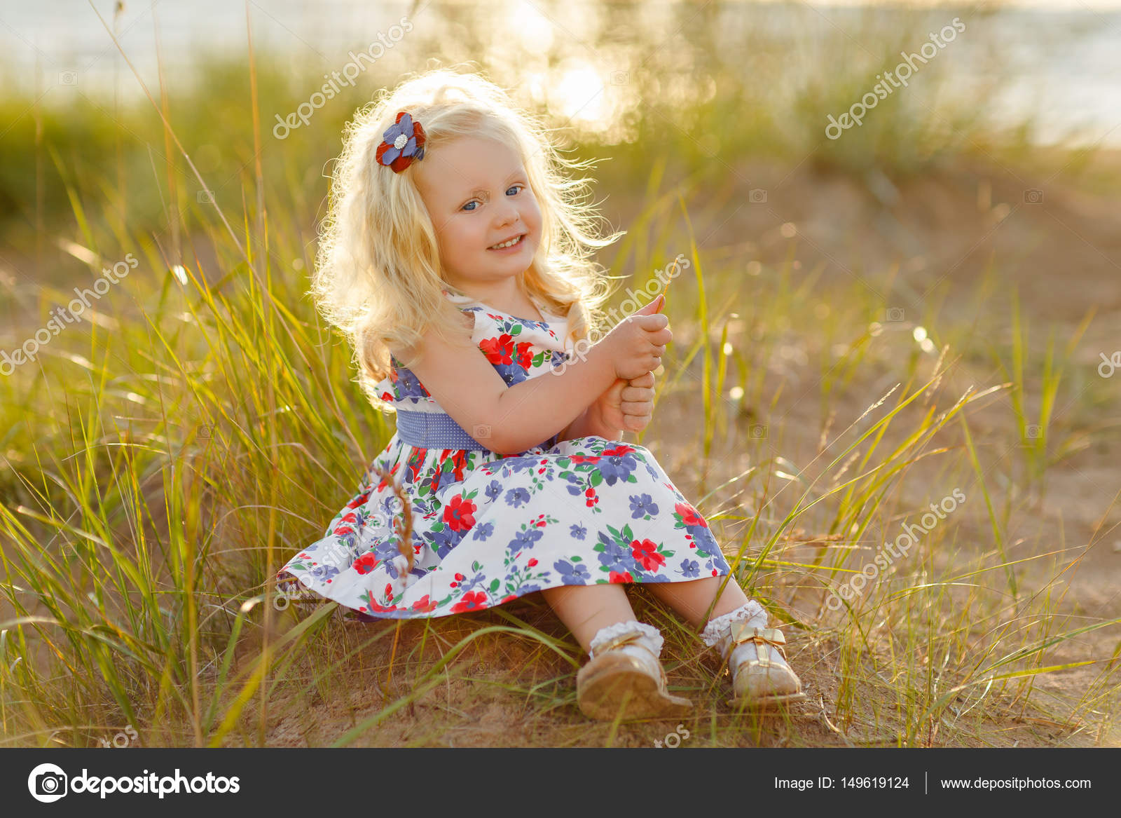 Little Curly Blonde Girl Sits And Smiles On Sand And Grass In Su Stock Photo By C Coy Creek