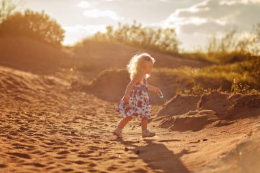 Küçük sarışın kız körfezin kıyısında kumun üzerinde çalışır. 