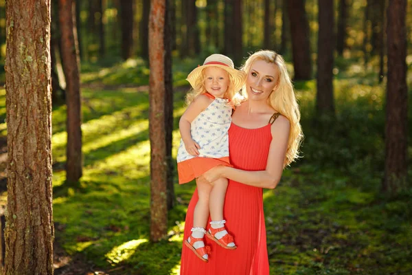 Kleines blondes Mädchen und ihre Mutter lächeln im Wald bei sonnigem Wetter — Stockfoto