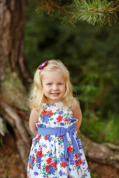在明亮的衣服和帽子在松树森林 smili 的金发小姑娘 — 图库照片