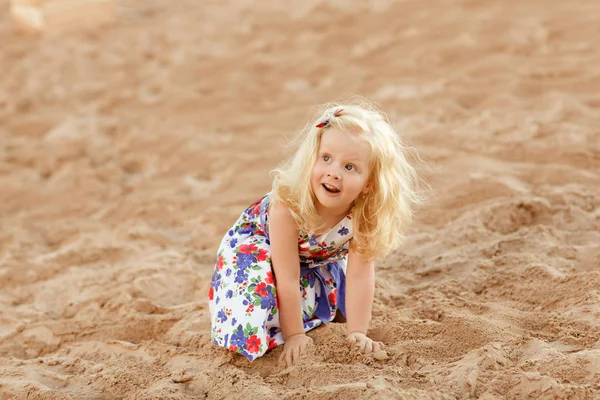 Blond meisje zit op de kust van de baai en speelt met s — Stockfoto