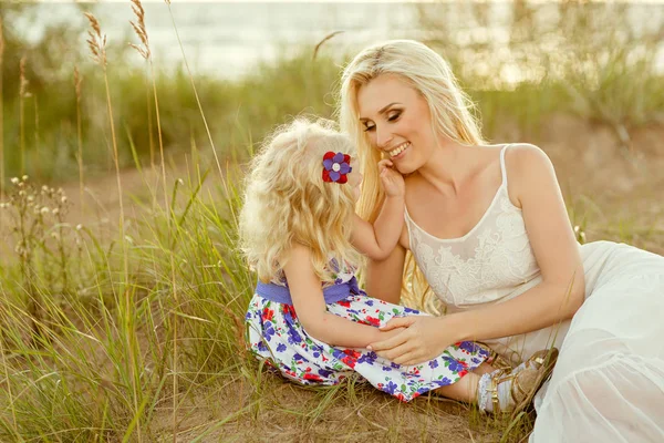 Uma menina loira e sua mãe estão sorrindo na areia e gras — Fotografia de Stock