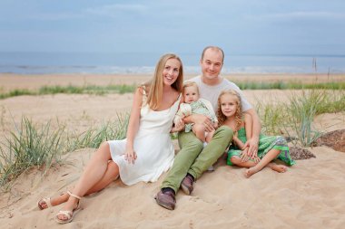 Anne, baba ve iki güzel kızı kum üzerine oturuyor