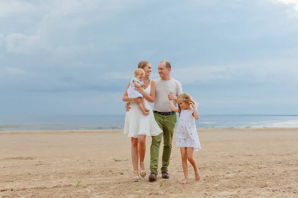 Mãe, pai e duas filhas encantadoras caminham ao longo da praia no — Fotografia de Stock