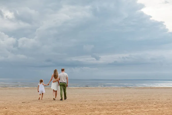 家族: お母さん、お父さんと女の子を見て海に向かって行きます。夏の曇りの天候で雲 — ストック写真